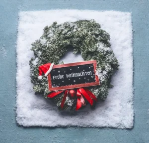 Weihnachtskranz mit roter Schleife und kleiner Tafel mit der Aufschrift „Frohe Weihnachten“, dekoriert mit Schnee – festliche Stimmung für den Weihnachtsgruss aus dem Stockhus auf der Fronalp.